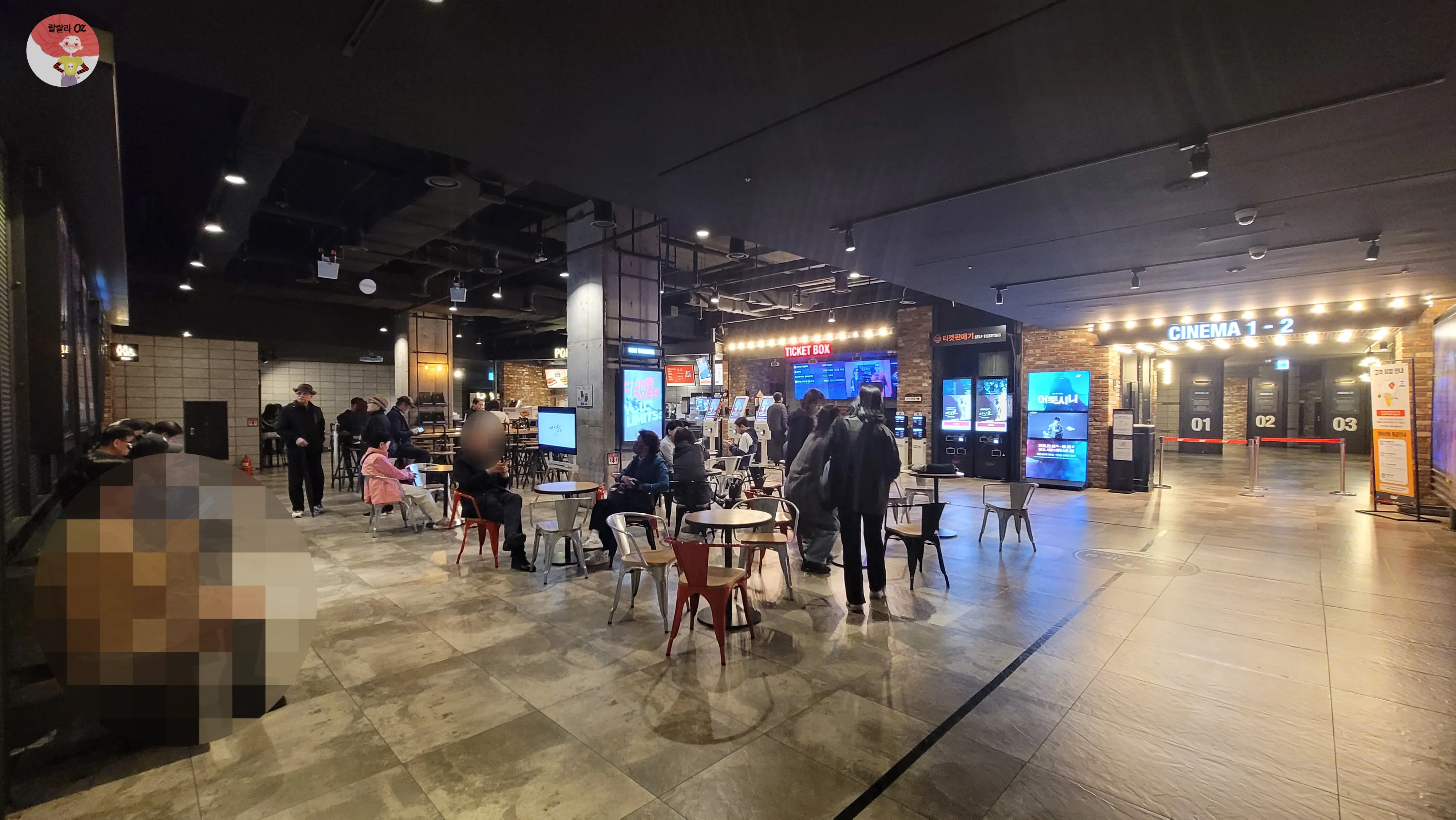서울 종로구 CGV 피카디리1958 극장 내부 전경, 따뜻한 조명 아래 현대적인 분위기의 로비 공간 곳곳에 작은 원형 테이블과 금속 의자, 서성이는 사람들