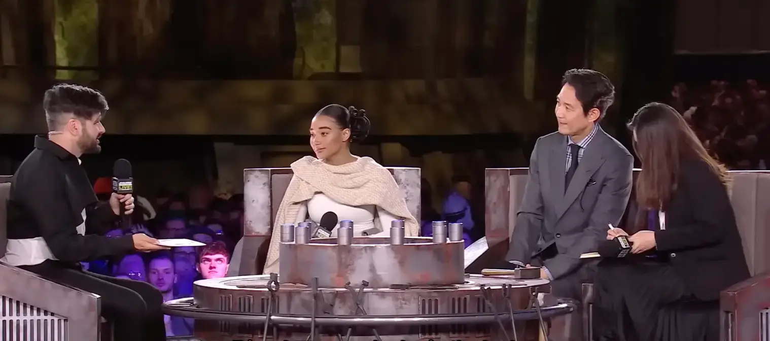 방송국 의자에 앉아 사회자와 이정재가 함께 말하는 모습