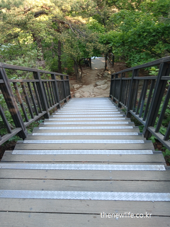 Wooden stairs with visible rocks at the bottom of descent&rdquo;- &ldquo;하단에 돌이 많은 불균형 계단 하강 구간&rdquo;