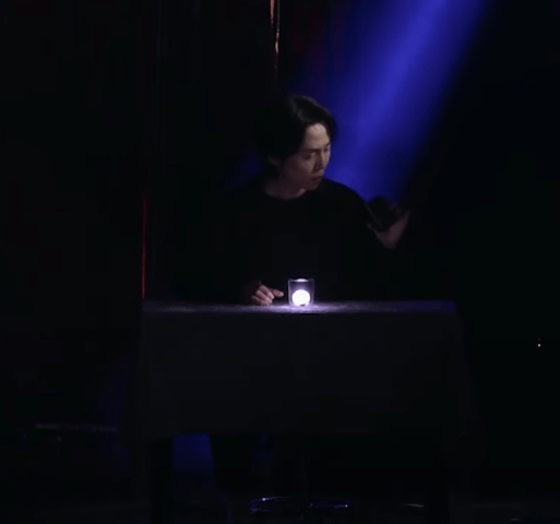 DK 마술사가 투명 유리잔안에 빛나는 공을 넣고 검정 컵을 들고 있다.