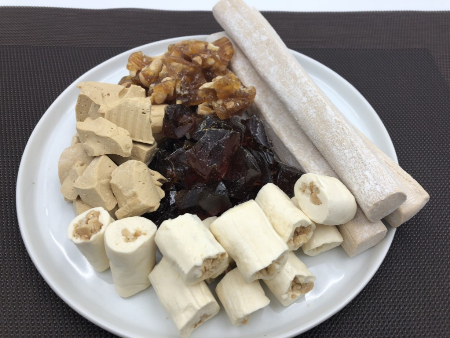 여러 가지 종류의 엿을 검은 바닥 위에 동그랗고 하얀 접시를 놓고 그 위에 담아놓고 찍은 사진