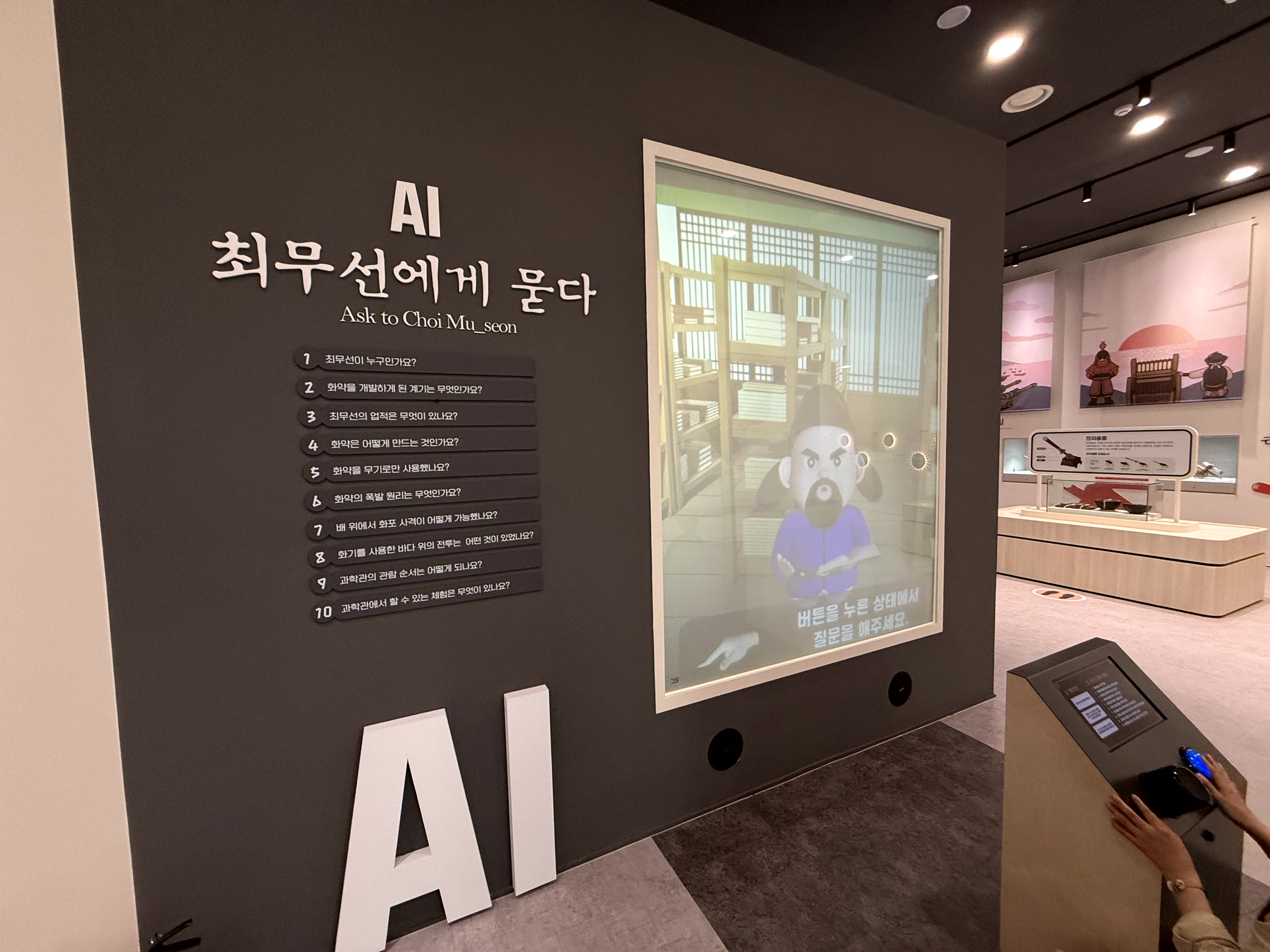 최무선과학관의 'AI 최무선에게 묻다' 인터랙티브 전시. 화면 속 AI 최무선 캐릭터에게 방문객이 질문을 하고 답변을 듣는 체험을 하고 있습니다.