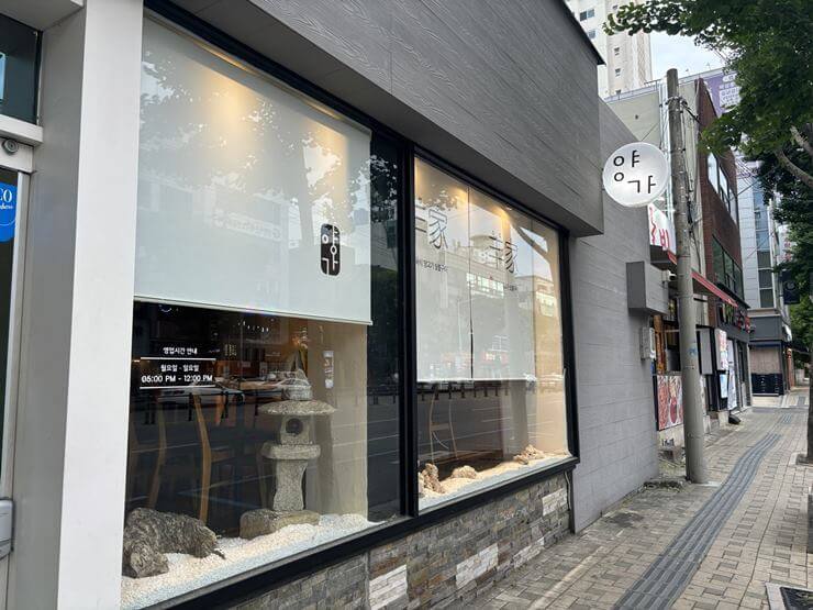 양가 식당 밖 모습이다. 근 유리창 2개가 있고 벽은 회색이다.