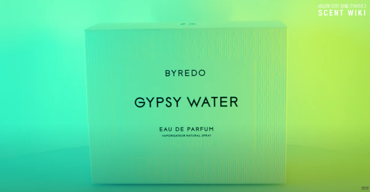 바이레도 집시 워터(BYREDO GYPSY WATER) 오 드 퍼퓸 패키지 박스 클로즈업. 미세한 세로 패턴이 들어간 고급스러운 화이트 박스 중앙에 브랜드명과 제품명이 검정 글씨로 인쇄되어 있으며, 배경은 청록색과 연두빛 그러데이션 조명으로 몽환적인 분위기를 연출함. 우측 상단엔 ‘SCENT WIKI’ 로고가 작게 표시되어 있음. 미니멀하고 세련된 감성의 향수 제품 이미지