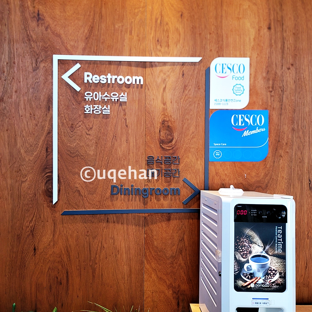 벽에 화장실표시와 음식 공간 대기공간 방향이 안내되고 있다. 오른쪽에는 무료 커피머신이 있다.