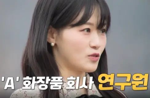 자연배경 검은리본이 달린 베이지색 원피스 긴웨이브머리를 하고 말하는 현숙의 옆모습 아래 'A'화장품 회사 연구원