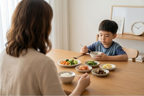엄마 어깨너머로 보이는 수저를 내려놓은 아들의 식탁