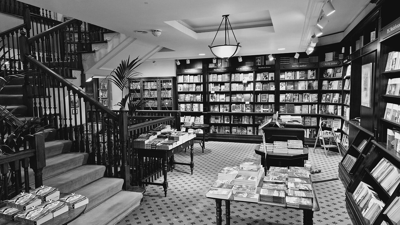 흑백사진. 왼쪽에 위에서 아래로 이어진 계단이 있고 어두운 색으로 책장이 벽을 둘러 있고 책장에는 책이 가득 꽂혀있다. 중간에 있는 공간에는 테이블이 곳곳에 놓여 있고 위에 책들이 놓여 있는 서점 내부