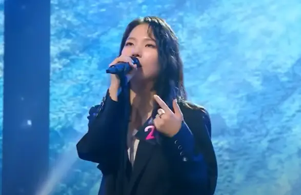 싱어게인3- 웨이브 진 검정색 긴머리로 오른손으로 마이크를 잡고 검정색 쟈켓을 입은채 눈을뜨고 노래하는 27호