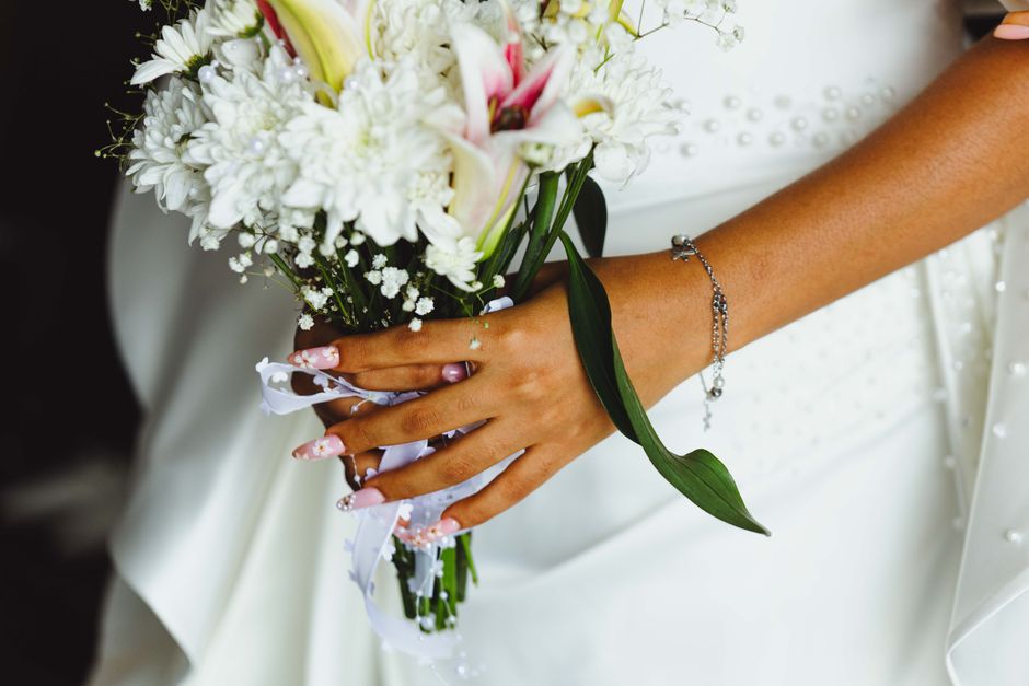 Close-up of a bridal bouquet with woman's hand showing manicured nails and bracelet.