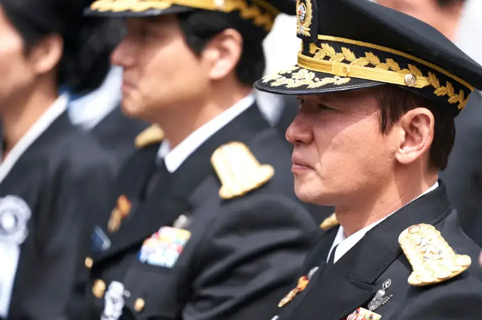 군인 제복과 모자를 쓰고 야외에서 앉아있는 전두광과 그옆 노태건