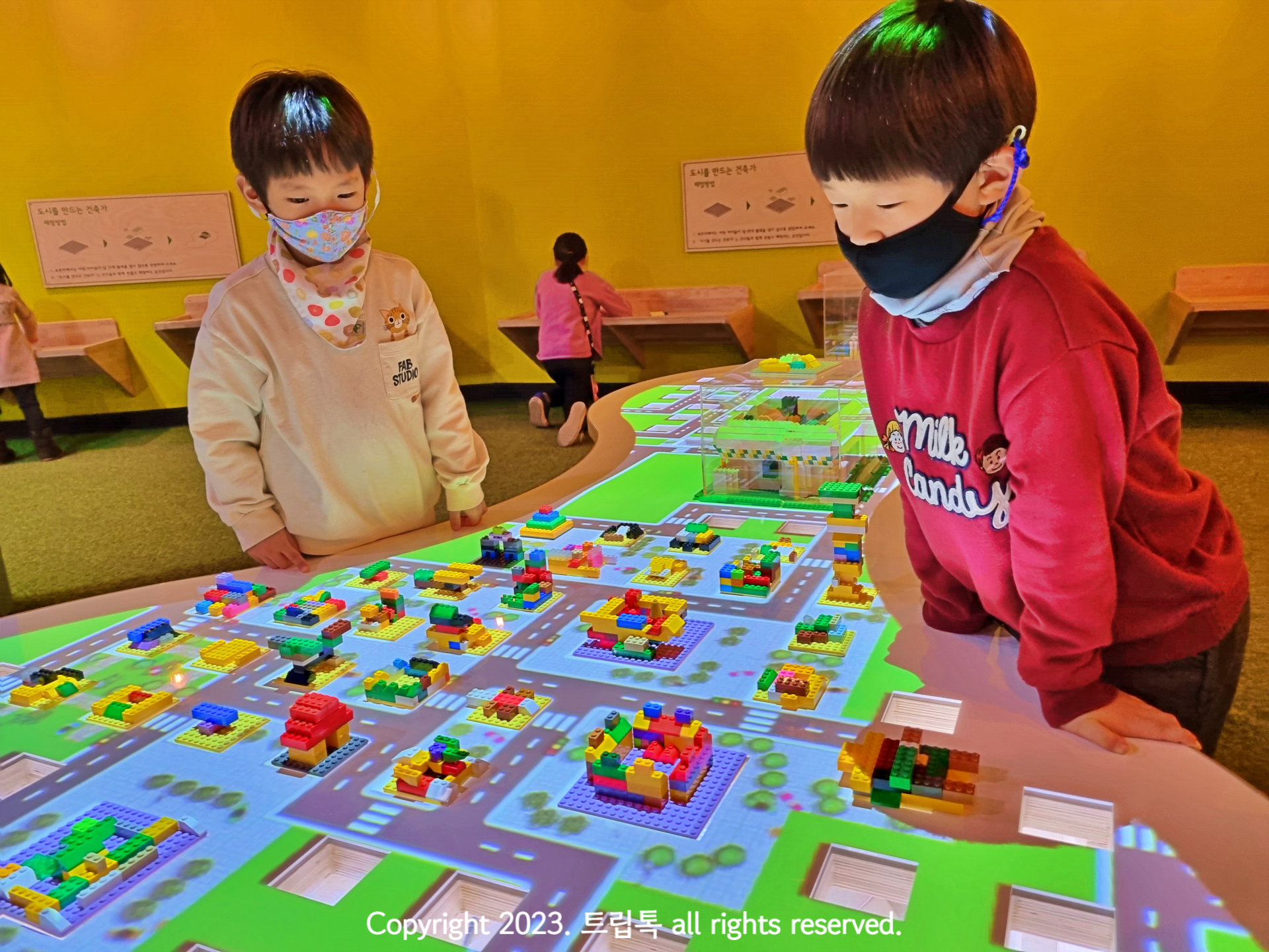 빛으로 이루어진 도로에 레고로 집을 지어 마을을 완선시키는 두명의 아이들