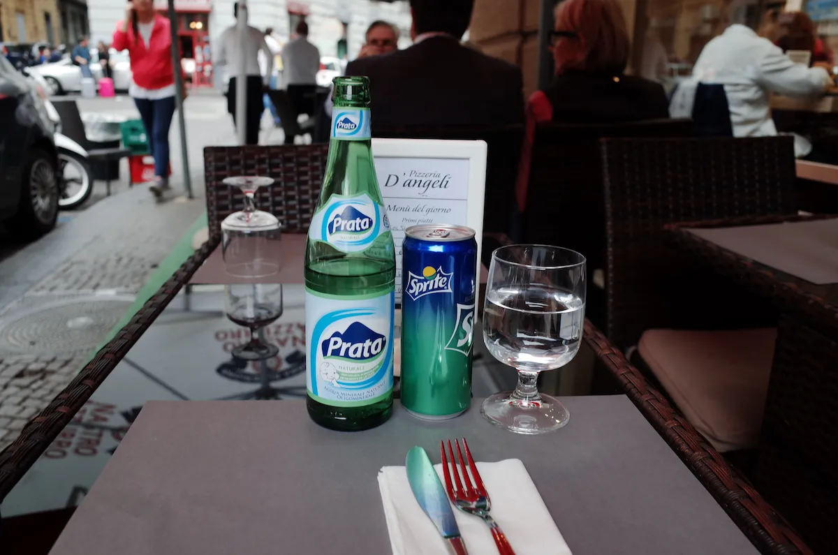 이탈리아 식당 야외 테이블에 놓인 프라타(Prata) 생수병과 스프라이트 캔, 정갈한 식기 세팅