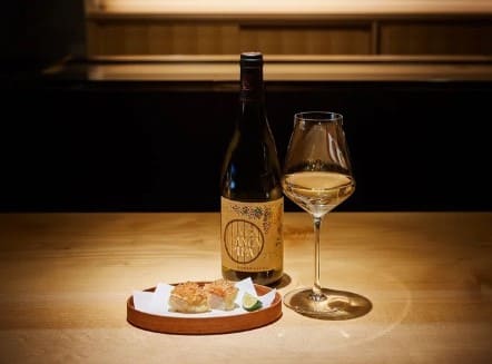 와인잔에 액체가 들어있고 옆에 조그만 접시에 음식물들이 있다.