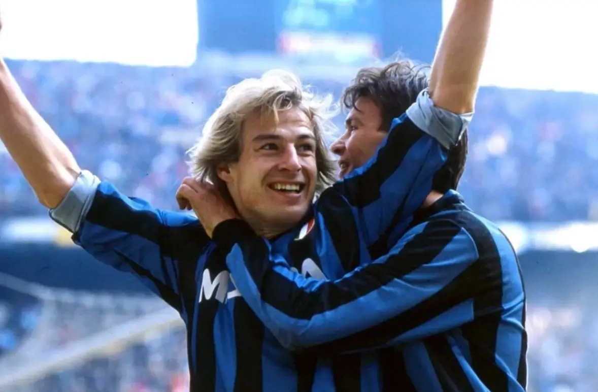 클린스만-파란색 유니폼을 입고 두손을 높이든채 미소짓는 클린스만과 그를 뒤에서 안아주는 동료