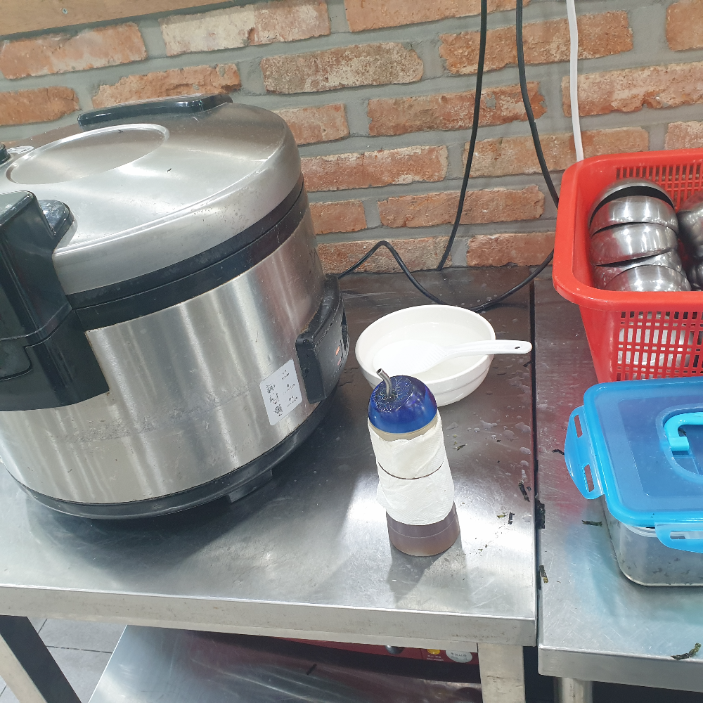 큰 은색 전기 밥통과 가운데 참기름 그리고 우측 파란통 안에 김가루