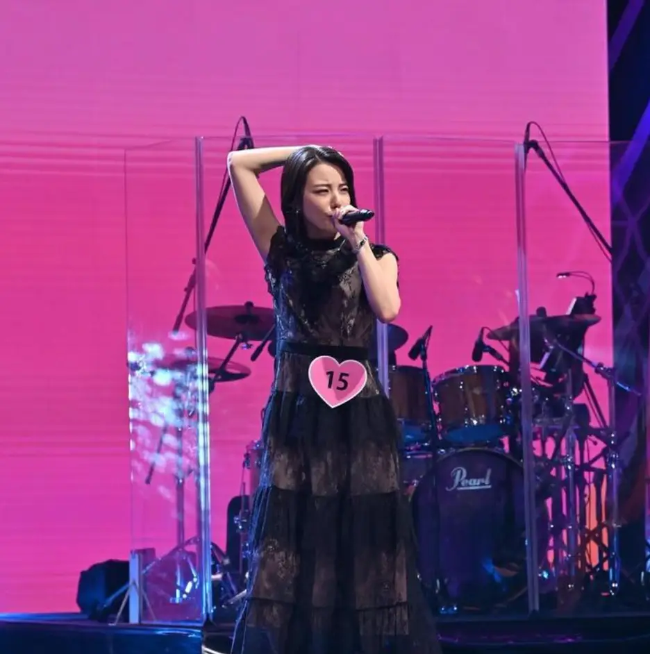 한일-붉은 무대 위 검은 긴 원피스를 입고 왼손으로 마이크를 든채 노래하고 있는 카노 미유