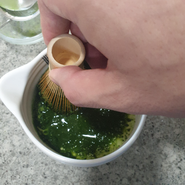 차선으로 말차를 푸는 모습 . 손으로 차선을 잡고 있다.