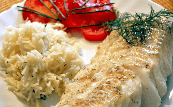 하얀 접시에 흰살 대구 스테이크와 흰쌀밥, 빨간 토마토 조각들이 있다. 대구 살 위에는 초록색 행신채들이 올려졌다.