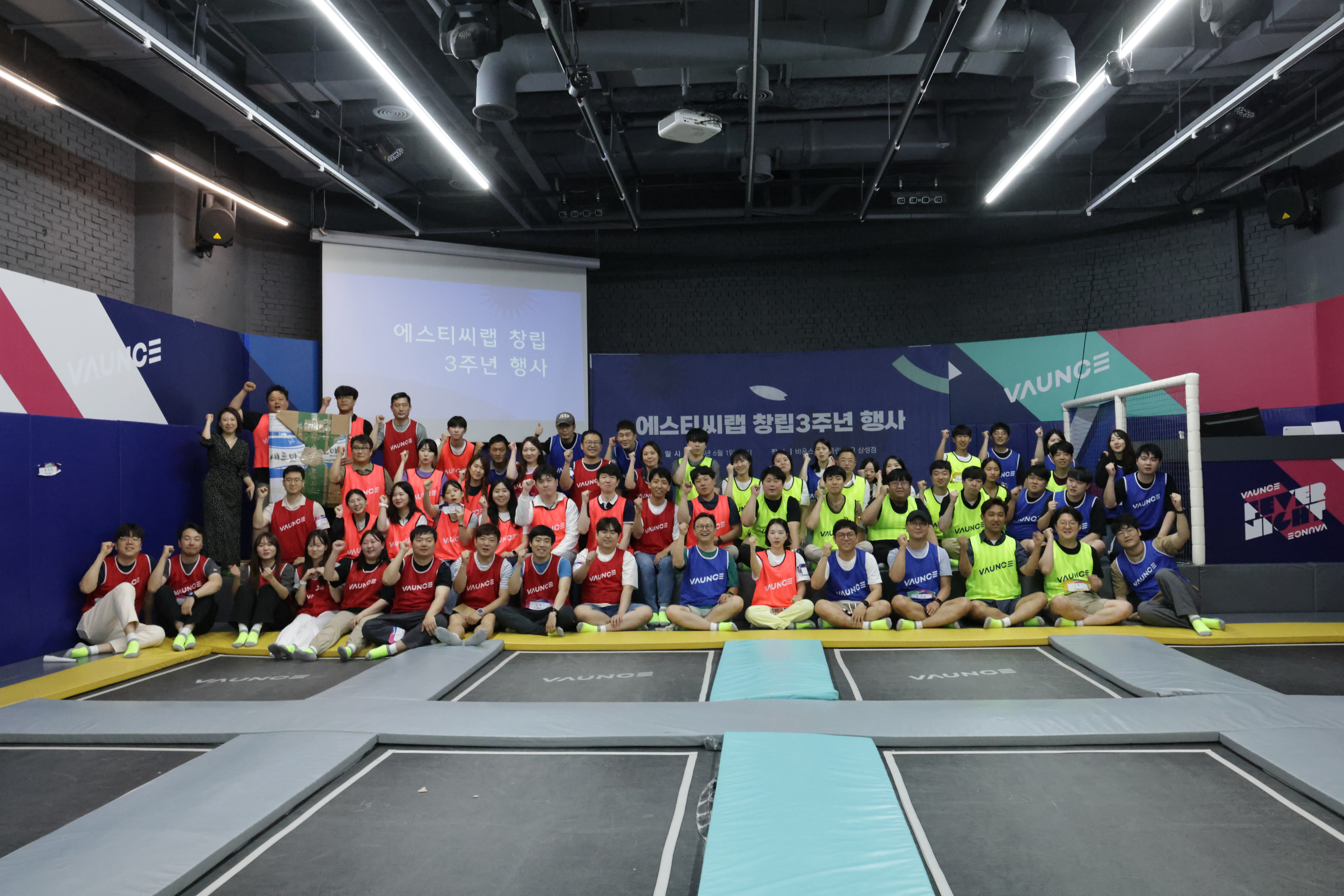 대략 50명의 사람들이 앞뒤 네줄로 나뉘어 단체사진을 찍기 위해 포즈를 취하고 있다.