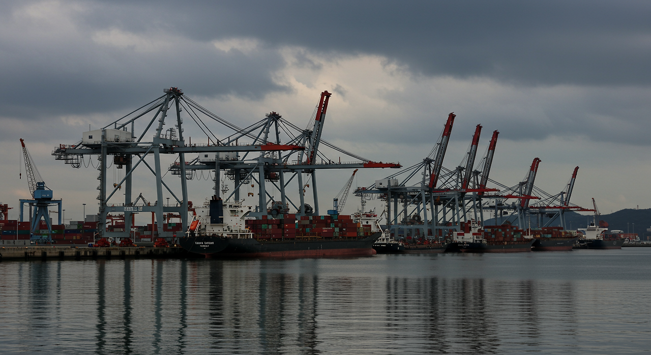 구름 낀 하늘 아래 정박 중인 컨테이너 선과 크레인이 있는 현대적인 항구