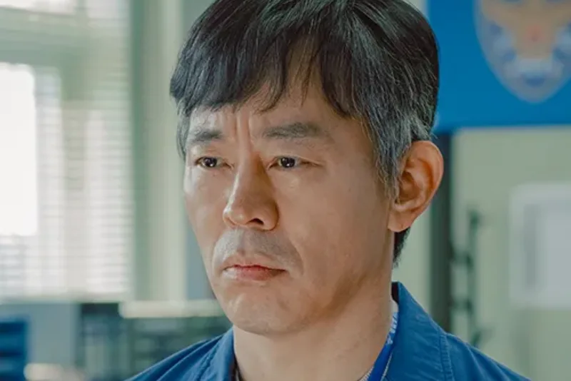 경찰서를 배경으로 파랑 자켓을 입고 목에 경찰신분증을 매고 누군가를 응시하는 새치가 많은 오팀장