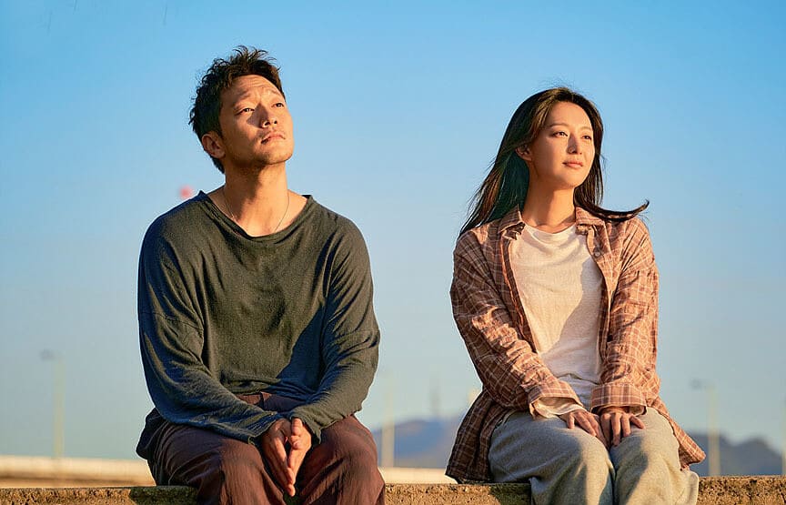 남녀주인공이 바닷가 계단에 걸터 앉아 석양을 바라보는 장면