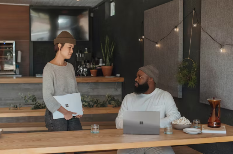 카페 또는 소형 사무실에서 두 명의 직원이 노트북과 문서를 앞에 두고 대화를 나누고 있는 모습.