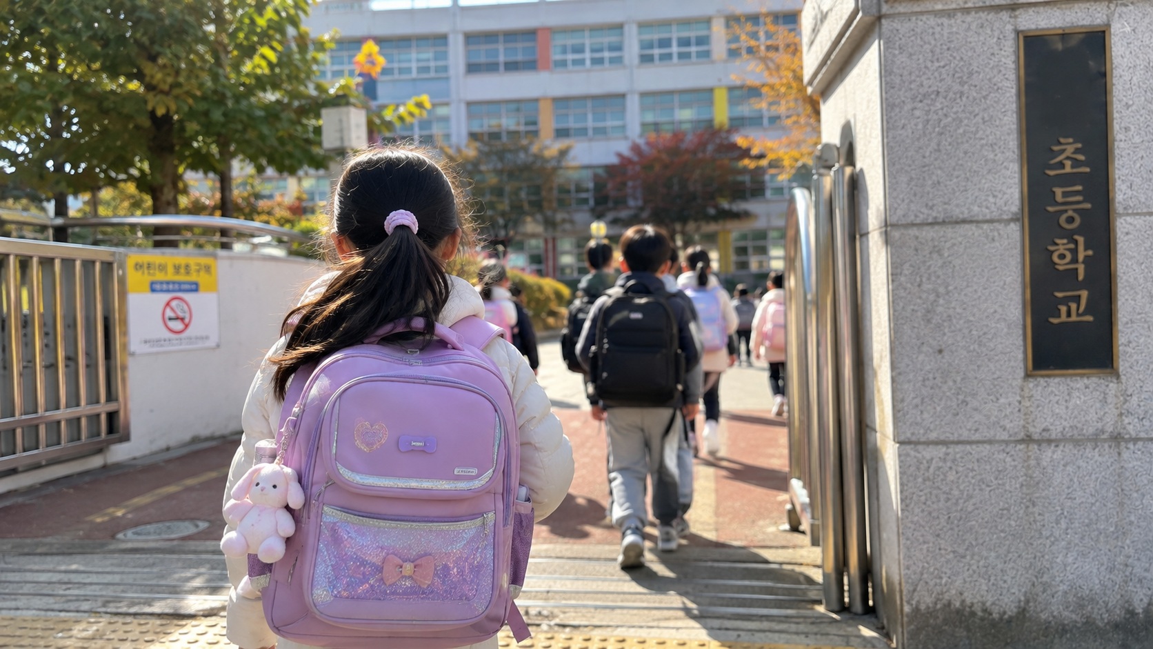 책가방을 메고 초등학교에 등교하는 저학년 아이의 뒷모습과 아동수당 지급연령 확대 관련 이미지