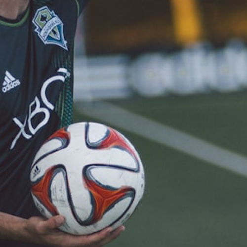 오른손으로 축구공을 안고 있는 유니폼 입은 선수