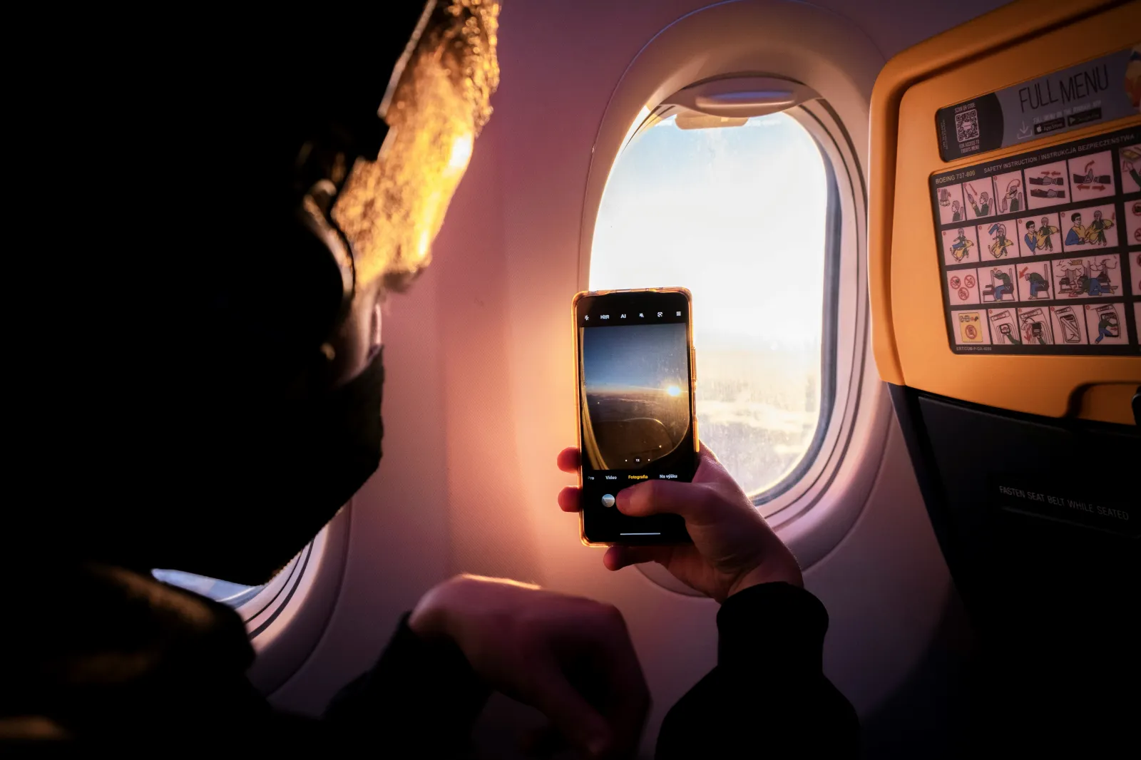 창가 쪽 비행기 안에서 휴대폰으로 떠오르는 태양을 찍는 모습