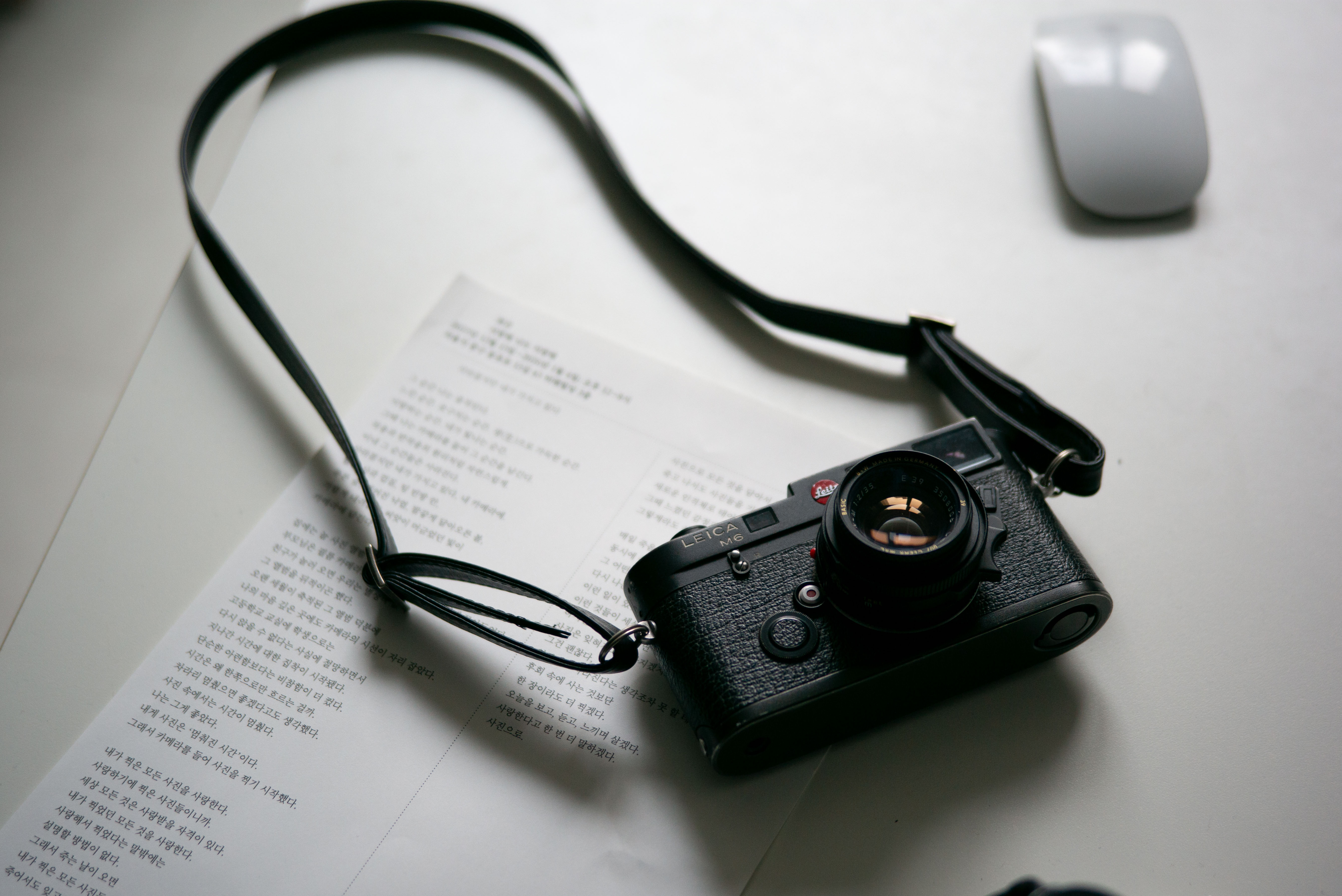 책상 위에 라이카 M6가 올려져있다. 가죽 스트랩이 부착되어 있으며 창가를 통해 들어오는 빛이 카메라를 향한다.