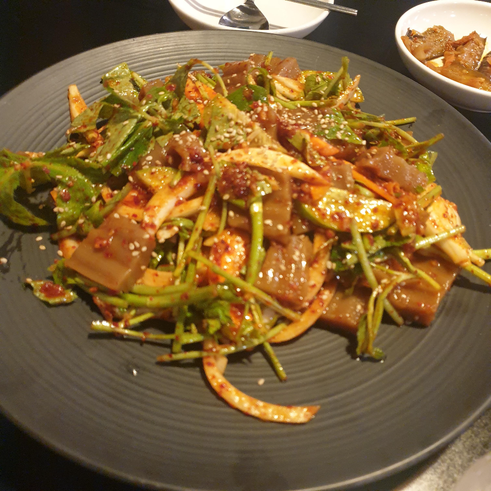 검은색 접시에 도토리묵이 담겨있다. 고추가루가 매워보인다.