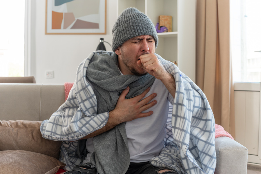 aching-ill-man-with-scarf-around-neck-wearing-winter-hat-wrapped-plaid-coughing-keeping-fist-close-mouth-sitting-couch-living-room-900