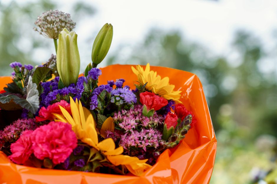 A colorful bouquet of assorted flowers wrapped in orange plastic, captured outdoors with a bright and romantic feel.