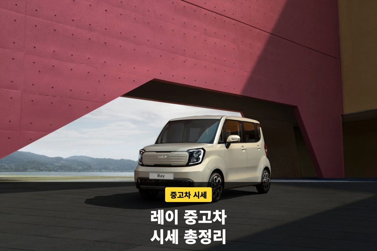 붉은 벽 앞에 서 있는 아이보리색 기아 레이 앞모습
