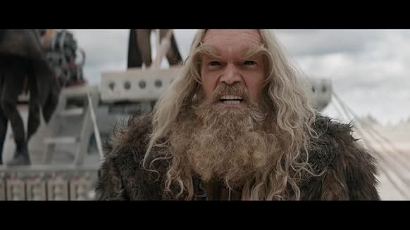 분노한 표정의 장발 캐릭터가 포효하는 장면, 바이킹 스타일 복장과 전쟁 분위기