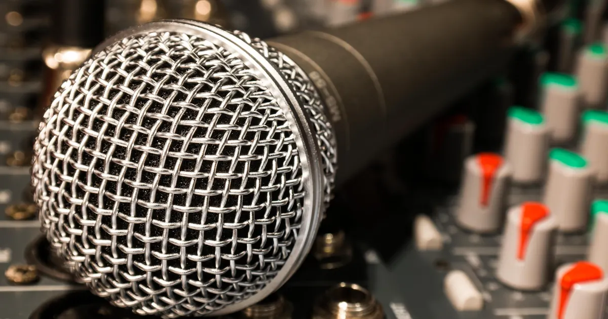 믹싱 콘솔 위에 놓인 다이나믹 마이크의 헤드 망 클로즈업과 배경에 보이는 믹서 노브들