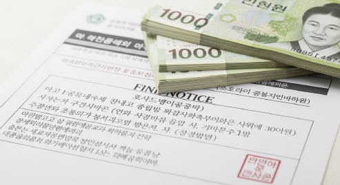 &lsquo;벌금 고지서&rsquo;를 상징하는 서류 위로 돈이 놓인 한국식 이미지