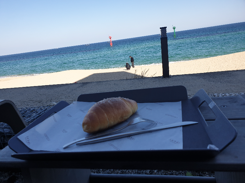 앞에 바다와 해변이 보인다. 트레이에 올려진 소금빵