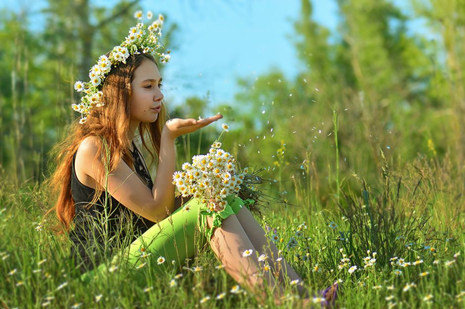 Woman in daisy wreath sitting in a lush green meadow during summer.