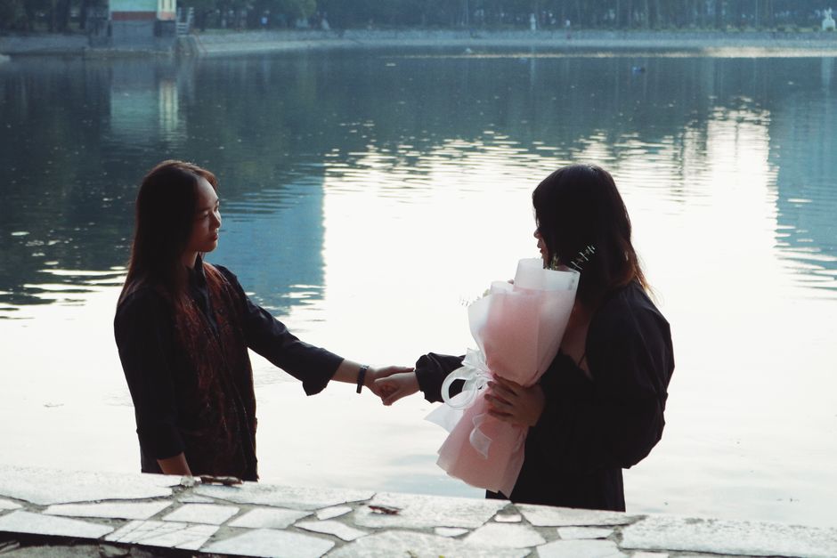 Two women exchanging flowers by a tranquil lake, capturing a serene autumn mood.