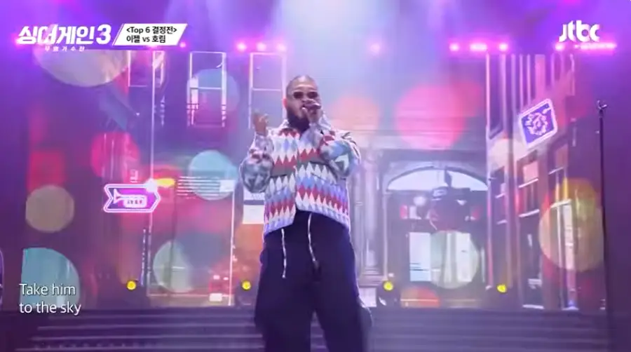 싱어게인3-
보라색배경 보라색 빨강색 격자무늬 외투 검은색 폴라티에 검은바지, 검은 선글라스 검은 마이크에 노래하는 16호 정면 모습