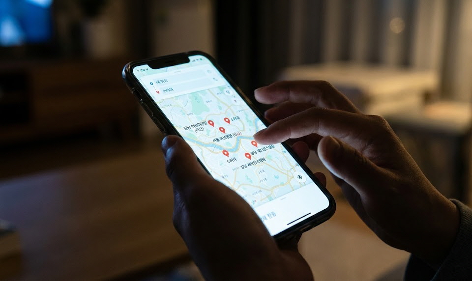 어두운 배경에서 병원 지도 위치가 표시된 스마트폰 화면을 확인하고 있는 부모의 손을 클로즈업한 모습.