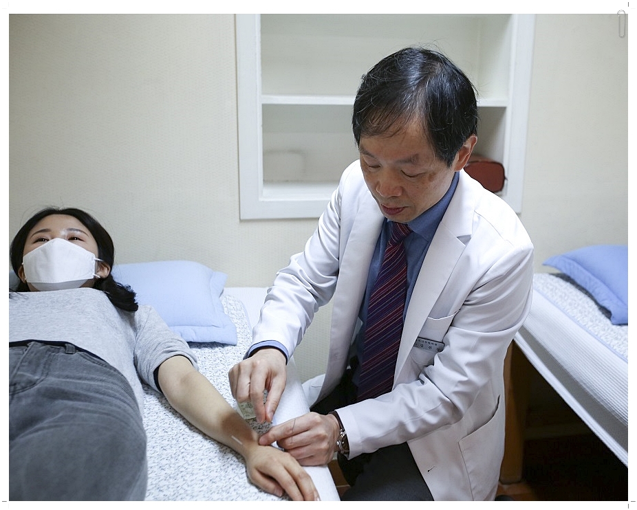 누워있는 환자의 손등에 침을 놓고 있는 한의사의 모습
