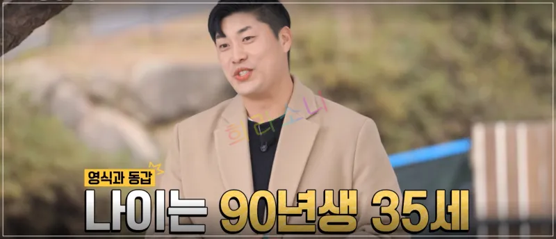 영철이 야외에서 서서 이야기하는 모습이다. 그는 짧은 머리에 베이지색 코트를 입고 있으며&amp;#44; 진지한 표정으로 인터뷰를 진행 중이다. 자막: 