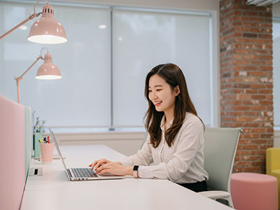 밝은 실내에서 노트북으로 온라인 신청 중인 젊은 한국인 여성&amp;#44; 웃으며 신청 과정을 진행 중인 모습
