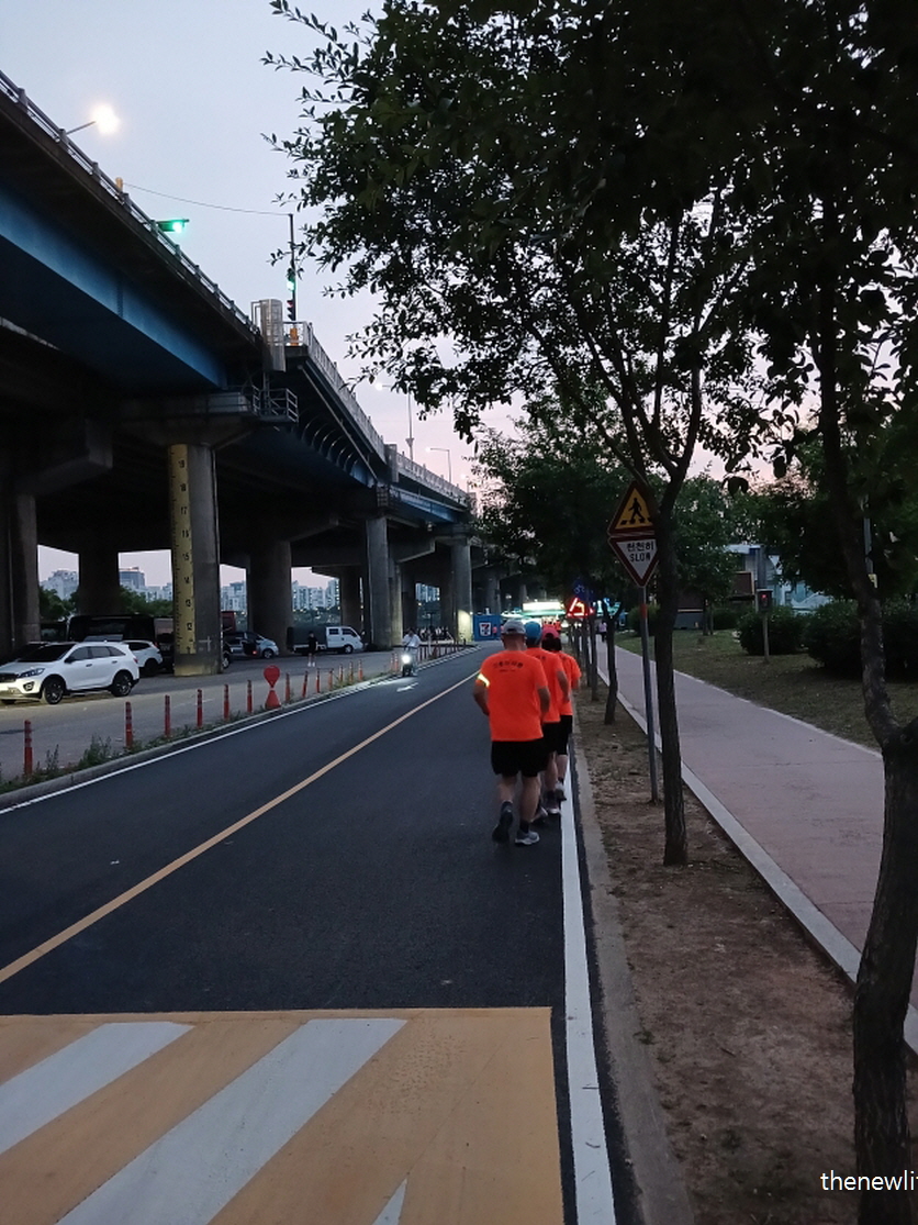 Group of men jogging along riverside road in the evening &ndash; demonstrating full-body benefits of jogging.-강변 도로에서 단체로 조깅 중인 남성들 (저녁 시간, 조깅 효과를 나타내는 장면)