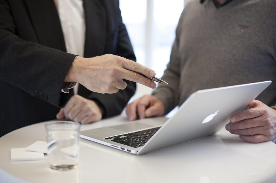 두 사람이 테이블에서 노트북을 보며 대화하고 있다