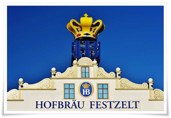푸른 하늘 배경에 노란색 왕관 장식이 있는 건물의 모습.
건물의 전면에 독일어로 호프브로이 축제텐트 라고 적혀있다.